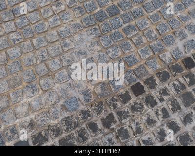 Eine Hochwinkeltextur eines Kopfsteinpflasters aus quadratischen Steinblöcken, die in einem diagonalen Rastermuster verlegt sind. Die Steine sind eine Mischung aus Grau, Sand und d Stockfoto