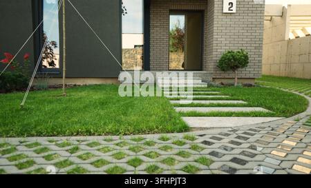 Moderner Hauseingang mit Ziegelfassade und gepflegtem grünen Rasen, der zu einem minimalistischen Betonweg führt Stockfoto