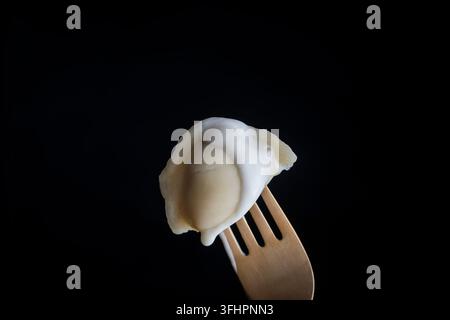 Ukrainische Knödel mit weißer saurer Sahne auf einer Gabel auf schwarzem Hintergrund, Nahaufnahme Stockfoto