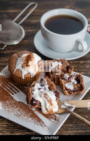 Süßer Kirschmuffin mit Eis und weißer Tasse mit Tee auf einem Holzhintergrund, Nahaufnahme Stockfoto
