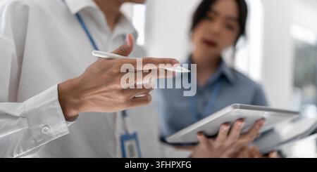 Zwei glückliche Geschäftsmenschen, asiatisches Team, arbeiten mit Digitaltablet-Technologie und diskutieren Finanzmarktdaten im Büro stehend. Stockfoto