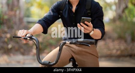 Geschäftsmann mit Fahrrad mit Smartphone außerhalb des Bürogebäudes. Mann, der mit dem Fahrrad pendelt, geht zur Arbeit. Umweltfreundliches Fahrzeug, nachhaltiger Lebensstil c Stockfoto