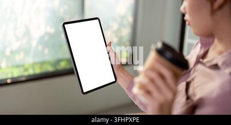 Modell einer Frau, die ein digitales Tablet mit leerem weißen Desktop-Bildschirm hält und eine Kaffeetasse hält Stockfoto