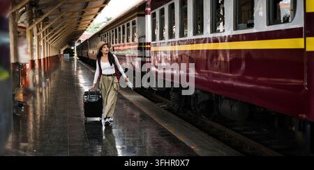 Junge Frau mit Koffer für einen Touristen-Abenteuerurlaub, der mit einem Zug reist. Konzept Transport Lebensstil aktiver Reise und Reiselebensstil. Stockfoto