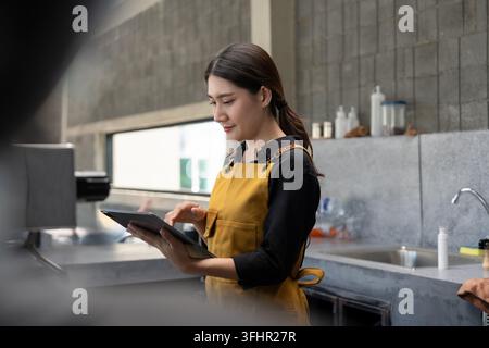 Junger Barista in gelber Schürze mit Tablet im modernen Coffee Shop Stockfoto