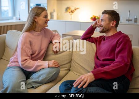 Lächelndes positives verheiratetes Paar, Mann und Frau, entspannt zusammen auf der Couch zu Hause und genießt das Gespräch. Stockfoto