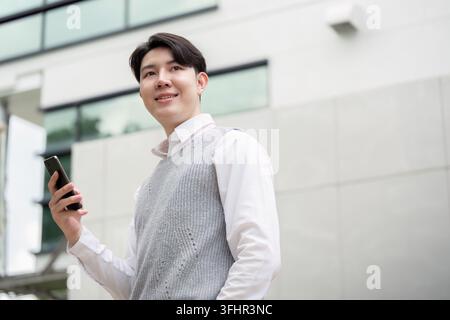 Selbstbewusster Junger Geschäftsmann, Der Ein Smartphone Vor Dem Modernen Bürogebäude Hält Stockfoto