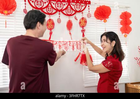 Ein älteres Paar dekoriert sein Zuhause fröhlich für das chinesische Neujahr und feiert Traditionen und familiäre Zusammenkunft. Stockfoto