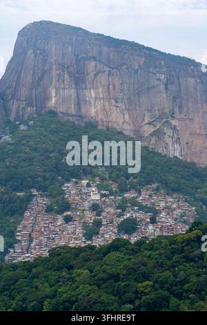 Blick auf den massiven Granitmonolithen der Pedra da Gavea, der über der dichten Hügelbebauung der Favela Rocinha thront, umgeben von üppigem tropischen Wald i Stockfoto
