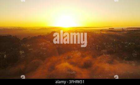 Sonnenaufgang über einem Vorstadtgebiet mit Nebel und warmem Glühen, das eine ruhige Morgenszene erzeugt, Drohnenfotografie - Samois-sur-Seine, Frankreich Stockfoto