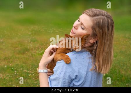 Zufriedene Frau mit ihrer roten Katze sitzt in einem Sessel auf dem Rasen Stockfoto