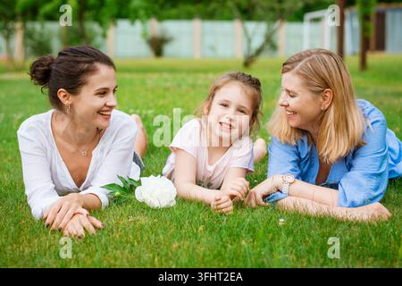 Glückliche dreigenerationale kaukasische Familie liegt zusammen auf dem Gras im Park, Mutter, Tochter und Großmutter haben Spaß, glücklich lächelnd, Familienbeziehung c Stockfoto