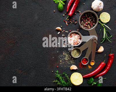 Vielfalt an farbenfrohen Gewürzen in Löffeln. Salzflocken, gemischter Pfeffer, Rosmarin, Basilikum und Knoblauch auf dunklem schwarzem Schieferhintergrund. Oben Stockfoto