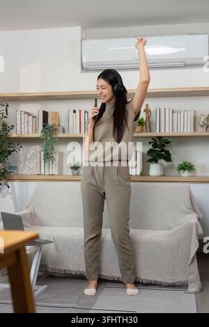 Energiegeladener Tanz- und Musikgenuss. Junge Frau, die Freude ausdrückt, während sie zu Hause singt. Stockfoto