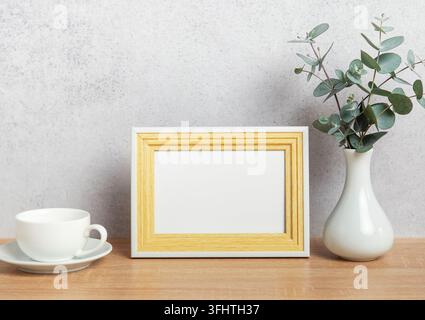 Leerer Fotorahmen, Kaffeetasse und Eukalyptuszweige auf dem Tisch Stockfoto