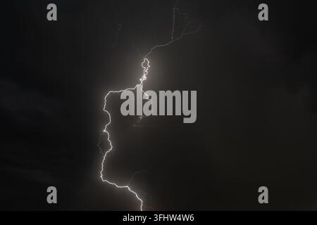 Ein dramatisches Gewitter erhellt den Nachthimmel über Dächern während einer mächtigen Blitzschau Stockfoto