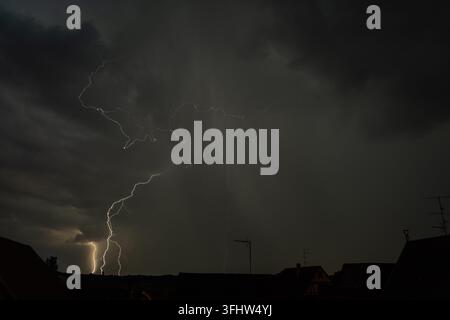 Ein dramatisches Gewitter erhellt den Nachthimmel über Dächern während einer mächtigen Blitzschau Stockfoto