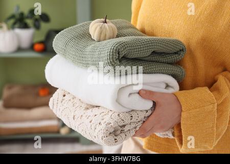 Herbstlicher Komfort und gemütliches Wohnleben, Person hält einen Stapel gefalteter Strickpullover und Decken mit einem kleinen dekorativen Kürbis für die Herbstsaison Stockfoto