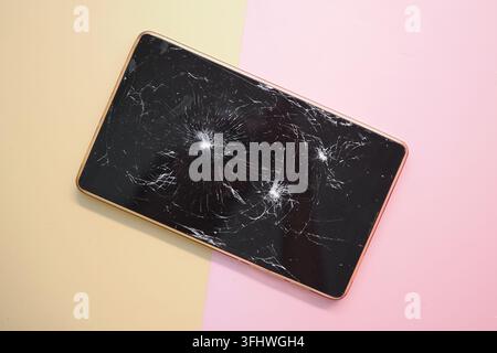 Zerbrochenes Mobiltelefon, das auf einer farbigen Oberfläche mit sichtbaren Rissen liegt Stockfoto