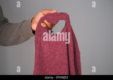 Hand, die ein Kleidungsstück mit einem Loch darin hält Stockfoto
