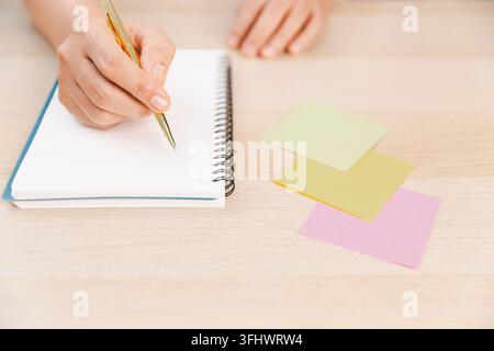Geschäftsprofi bereitet Notizen in einem Spiralnotizbuch neben bunten Haftnotizen auf einem Schreibtisch vor, was Planung, Organisation, Erinnerungen, Pro darstellt Stockfoto