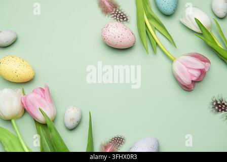 Festliche osterbordkomposition mit bunten Eiern und Tulpen auf pastellgrünem Hintergrund Stockfoto