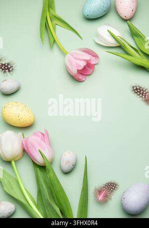 Festliche osterbordkomposition mit bunten Eiern und Tulpen auf pastellgrünem Hintergrund Stockfoto