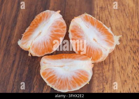 Geschälte Mandarinenstücke mit hellorangen Segmenten und weißem Fruchtfleisch auf einer Holzoberfläche. Stockfoto