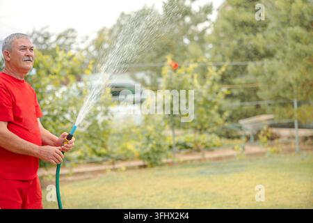 Mann bewässert den Rasen. Bewässerungssystem-Rasensprinkler sprüht Wasser über frisches grünes Gras im Garten an einem Sommermorgen bei leichtem Wetter Stockfoto