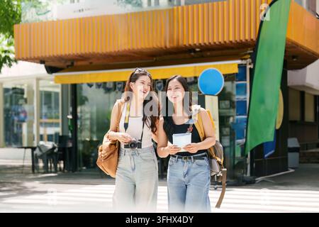 Zwei fröhliche junge Frauen gehen mit Rucksäcken und einer Karte durch die Stadt, aufgeregt über ihr Reiseabenteuer. Stockfoto