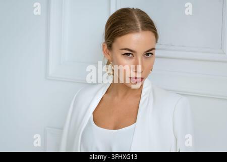 Porträt einer jungen blonden Frau in weißer Kleidung vor dem Hintergrund eines weißen Interieurs Stockfoto