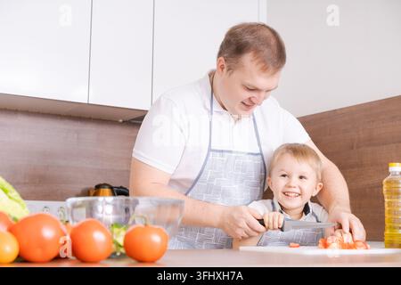 Glückliche Familienvater mit Sohn bereitet Gemüsesalat zu Hause zu, Gemüse Stockfoto
