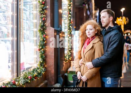 Ein Mann und eine Frau stehen vor einem Fenster mit Weihnachtsdekoration Stockfoto