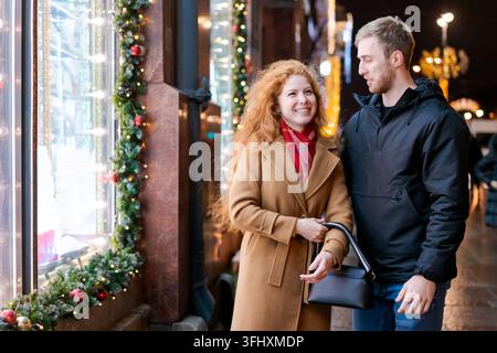 Ein Mann und eine Frau stehen vor einem Fenster mit Weihnachtsdekoration Stockfoto