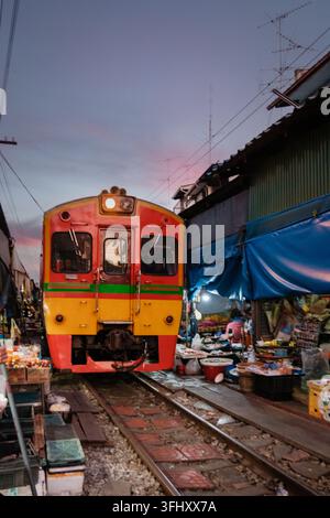 Farbenfroher Zug, der den Maeklong-Bahnhofmarkt in Thailand im Abenddämmerung durchfährt Stockfoto