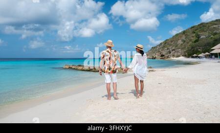 Ein paar Spaziergänge Hand in Hand entlang der weichen Sandküste von Porto Mari Beach in Willemstad, Curacao. Das türkisfarbene Wasser und die flauschigen Wolken bilden einen stu Stockfoto