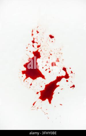 Rote Blutspritzer und Flecken auf weißem Hintergrund, die ein dramatisches Muster mit starkem konzeptionellem Kontrast erzeugen Stockfoto