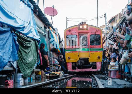 Maeklong Railway Market, Thailand, am 5. Dezember 2025 ziehen Händler schnell zur Seite, während ein Zug durch den belebten Markt fährt. Eine fesselnde Szene Stockfoto