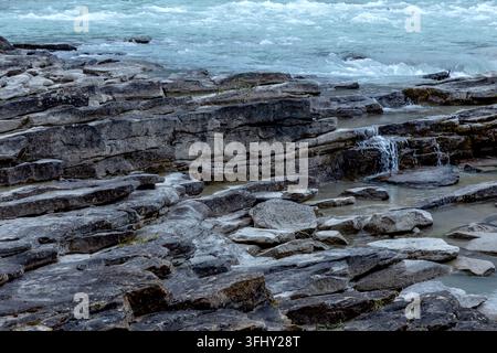 Mächtiger Wasserfall stürzt über geschichtete Felsen, umgeben von üppigem grünem Wald, Athabasca-Fälle, Jasper-Park, Alberta, Kanada Stockfoto