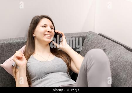 Eine Frau sitzt auf einer Couch und telefoniert mit ihrem Handy Stockfoto