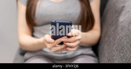 Eine Frau sitzt auf einer Couch und benutzt ihr Handy Stockfoto