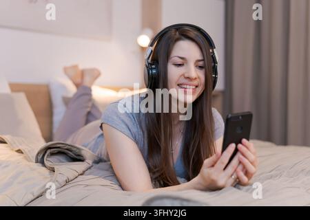 Eine Frau liegt auf einem Bett und benutzt ihr Handy Stockfoto