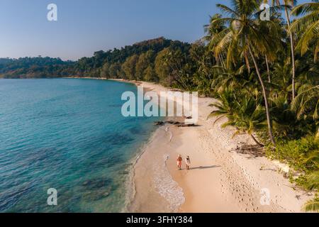 Erleben Sie einen ruhigen Morgen, während zwei Reisende Hand in Hand entlang des weichen Sandes von Takhian Beach gehen, umgeben von wogenden Palmen und Kristallkellen Stockfoto