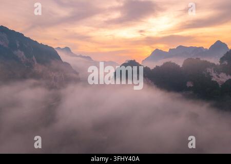 Erleben Sie den atemberaubenden Sonnenaufgang im Khao Sok National Park Thailand, wo leuchtende Sonnenaufgangsfarben mit nebeligen Wolken über ruhigen Tälern und majestätischen Tälern verschmelzen Stockfoto