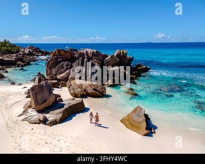 Ein Paar genießt einen gemütlichen Spaziergang entlang der unberührten Küste des Anse Cocos Strandes, umgeben von atemberaubenden Granitfelsen und türkisfarbenem Wasser. Perfekt Stockfoto