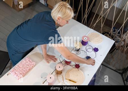 Der Lehrer bereitet sich auf den Häkelkurs vor. Frau, die Fadenhaken und Produktmuster auf dem Tisch auslegt. Stockfoto