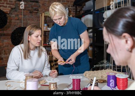 Drei Frauen basteln mit bunten Garnen und Häkelhaken am Tisch in gemütlicher Werkstatt. Stockfoto