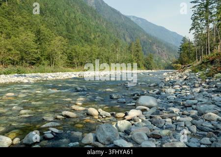 Ein ruhiger Bergfluss fließt durch einen üppigen Wald mit einem umgestürzten Baum am felsigen Ufer, Asha Mahakaleshwar Tempel, 22580 Coquihalla Hwy, Hope, BC Stockfoto
