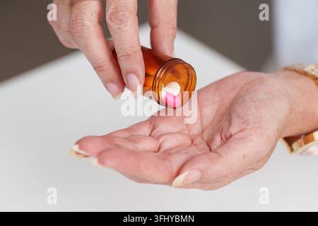 Eine Person, die rosafarbene Kapseln aus einer verschreibungspflichtigen Flasche in die Hand gießt und dabei das Medikamentenmanagement betont. Stockfoto