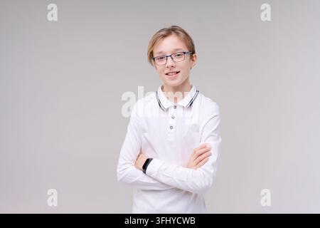 Zuckender kaukasischer Junge, zweifelende zuckende Schultern, Schuljunge, Teenager mit Brille in einem weißen T-Shirt. Der Junge wählt auf einem grauen Hintergrund. Stockfoto